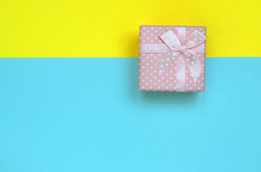 Küçük pembe hediye kutusu yalan doku arka planda moda pastel mavi ve sarı renkler kağıt en az kavramında.