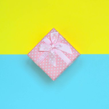 Küçük pembe hediye kutusu yalan doku arka planda moda pastel mavi ve sarı renkler kağıt en az kavramında.