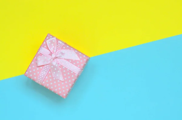 小粉色礼品盒位于时尚柔和的蓝色和黄色的颜色纸的纹理背景最小概念 — 图库照片