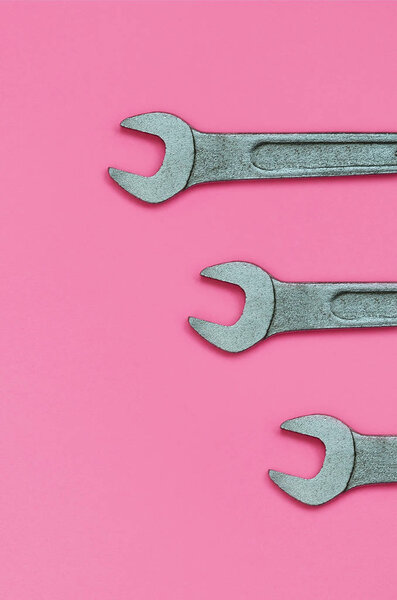 Three metallic spanners lie on texture background of fashion pastel pink color paper in minimal concept.