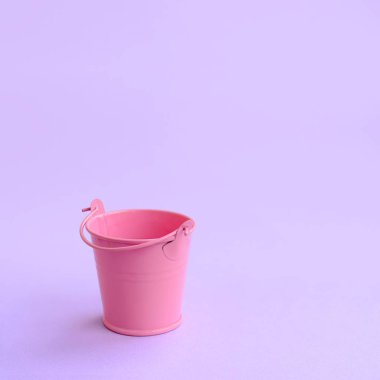 Bir minyatür boş pembe kova bir menekşe pastel arka plan üzerinde yatıyor. En az kavramı.
