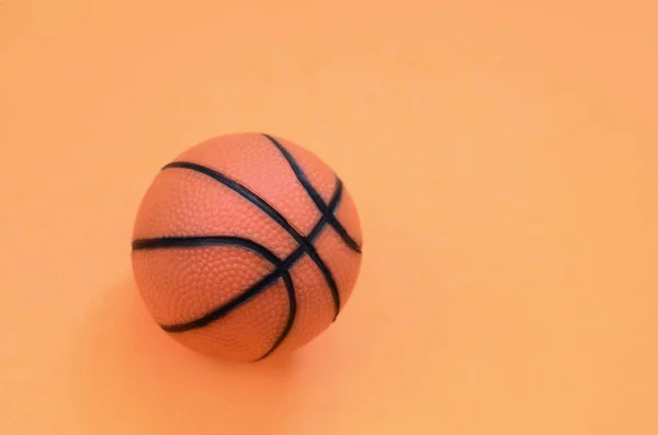 Small orange ball for basketball sport game lies on texture background of fashion pastel orange color paper in minimal concept.