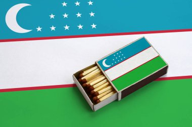 Özbekistan bayrağı açık bir kibrit kutusu içinde gösterilen hangi dolu maçlar ve büyük bir bayrak üzerinde yatıyor.