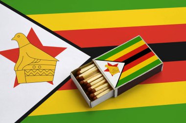 Zimbabve bayrağı açık bir kibrit kutusu içinde gösterilen hangi dolu maçlar ve büyük bir bayrak üzerinde yatıyor.