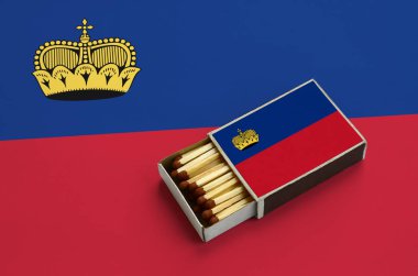 Lihtenştayn bayrağı açık bir kibrit kutusu içinde gösterilen hangi dolu maçlar ve büyük bir bayrak üzerinde yatıyor.