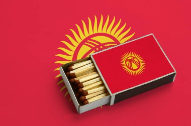 Kırgızistan bayrağı açık bir kibrit kutusu içinde gösterilen hangi dolu maçlar ve büyük bir bayrak üzerinde yatıyor.