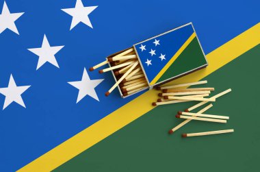 Solomon Adaları bayrağı bir kibrit kutusu içinden birkaç sonbahar eşleşir ve büyük bir bayrak üzerinde yatıyor açık gösterilir.