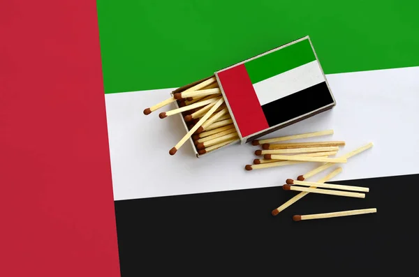 United Arab Emirates flag  is shown on an open matchbox, from which several matches fall and lies on a large flag.