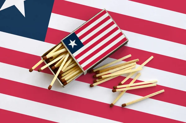 Liberya bayrağı bir kibrit kutusu içinden birkaç sonbahar eşleşir ve büyük bir bayrak üzerinde yatıyor açık gösterilir.