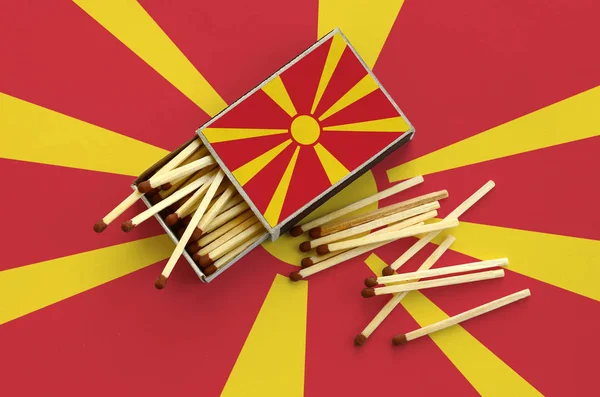 Macedonia flag  is shown on an open matchbox, from which several matches fall and lies on a large flag.