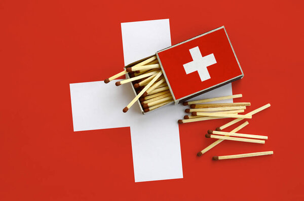 Switzerland flag  is shown on an open matchbox, from which several matches fall and lies on a large flag.