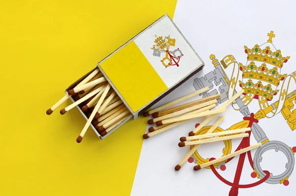 Vatikan şehir devleti bayrağı bir kibrit kutusu içinden birkaç sonbahar eşleşir ve büyük bir bayrak üzerinde yatıyor açık gösterilir.