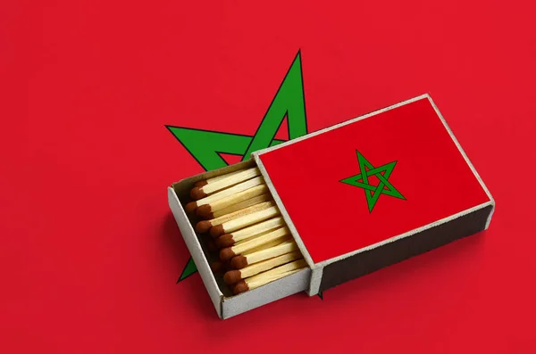 Morocco flag  is shown in an open matchbox, which is filled with matches and lies on a large flag.