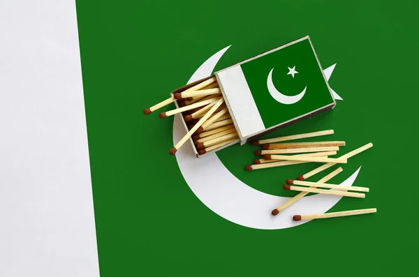 Pakistan flag  is shown on an open matchbox, from which several matches fall and lies on a large flag.