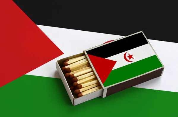 Western Sahara flag  is shown in an open matchbox, which is filled with matches and lies on a large flag.