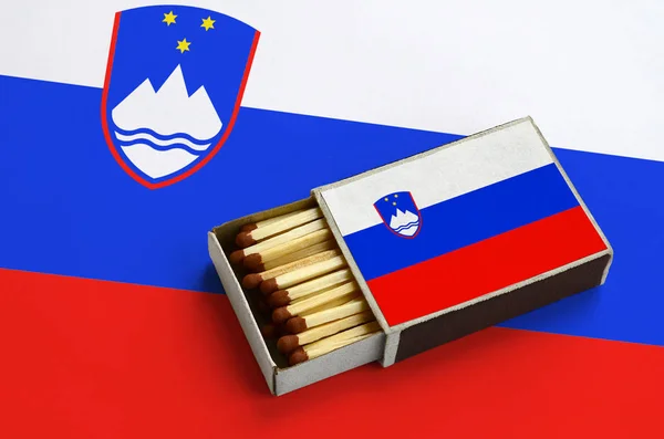 Slovenia flag  is shown in an open matchbox, which is filled with matches and lies on a large flag.