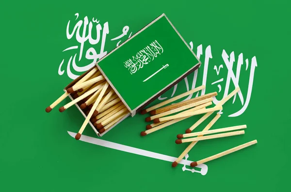Suudi Arabistan bayrağı bir kibrit kutusu içinden birkaç sonbahar eşleşir ve büyük bir bayrak üzerinde yatıyor açık gösterilir.