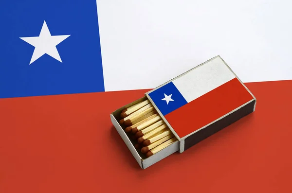 Chile flag  is shown in an open matchbox, which is filled with matches and lies on a large flag.