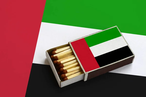 United Arab Emirates flag  is shown in an open matchbox, which is filled with matches and lies on a large flag.