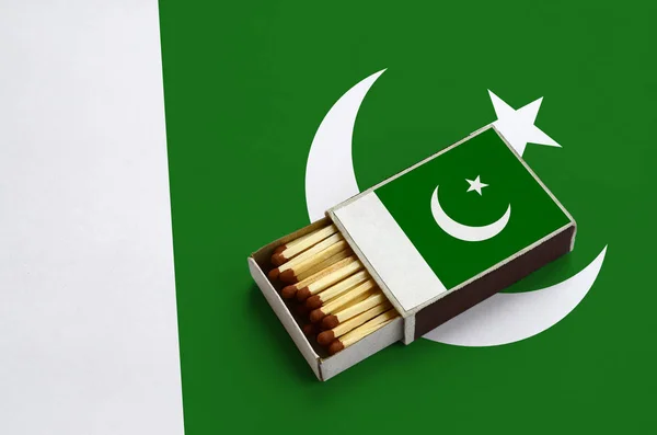 Pakistan flag  is shown in an open matchbox, which is filled with matches and lies on a large flag.