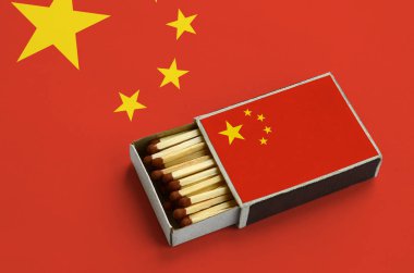 Çin bayrağı açık bir kibrit kutusu içinde gösterilen hangi dolu maçlar ve büyük bir bayrak üzerinde yatıyor.