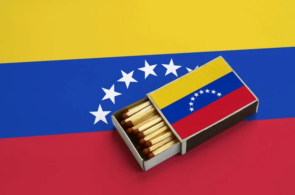 Venezuela flag  is shown in an open matchbox, which is filled with matches and lies on a large flag.
