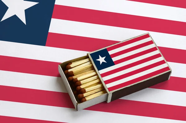 Liberya bayrağı açık bir kibrit kutusu içinde gösterilen hangi dolu maçlar ve büyük bir bayrak üzerinde yatıyor.