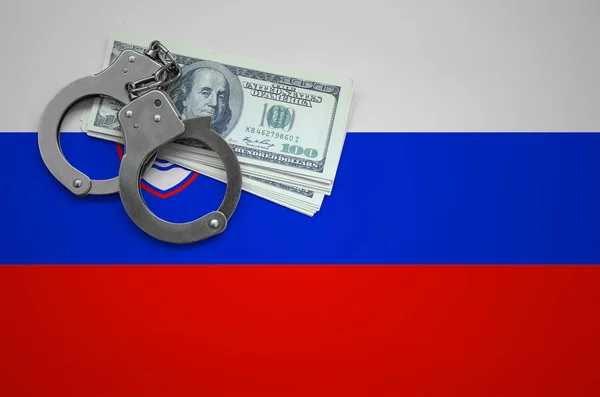 Slovenia flag  with handcuffs and a bundle of dollars. The concept of breaking the law and thieves crimes.