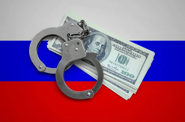 Russia flag  with handcuffs and a bundle of dollars. Currency corruption in the country. Financial crimes.