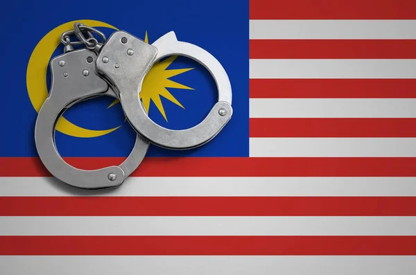 Malaysia flag  and police handcuffs. The concept of crime and offenses in the country.