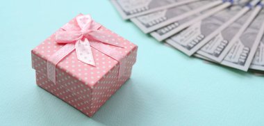 Yüz dolar faturaları üzerinde bir açık mavi renkli yakınındaki pembe noktalı hediye kutusu yatıyor.