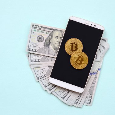 Bir akıllı telefon ve açık mavi arka planı üzerinde yüz dolar faturaları üzerinde Bitcoins yalan.