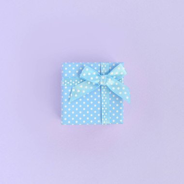 Küçük mavi hediye kutusu kurdele ile mor bir arka plan üzerinde yatıyor. Üstten görünüm minimalizm düz yatıyordu.