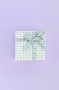 Küçük beyaz hediye kutusu kurdele ile mor bir arka plan üzerinde yatıyor. Üstten görünüm minimalizm düz yatıyordu.