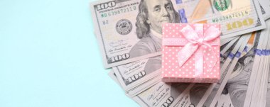Yüz dolar faturaları üzerinde bir açık mavi renkli yakınındaki pembe noktalı hediye kutusu yatıyor.