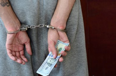 Kelepçeli elleriyle gri pantolon tutuklanan bir adam para büyük miktarda tutar. Arkadan görünüm.