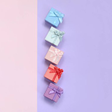 Küçük hediye kutuları farklı renklerde kurdeleler yalanlar üzerine mor ve pembe renkli bir arka planla ile.
