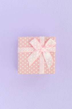 Küçük pembe hediye kutusu kurdele ile mor bir arka plan üzerinde yatıyor. Üstten görünüm minimalizm düz yatıyordu.