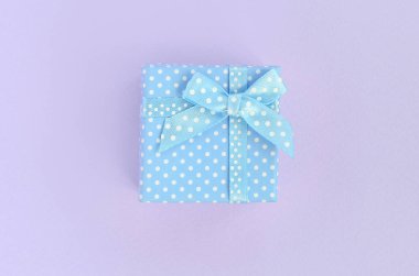 Küçük mavi hediye kutusu kurdele ile mor bir arka plan üzerinde yatıyor. Üstten görünüm minimalizm düz yatıyordu.