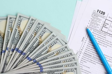 1120 formu yalan yüz dolar faturaları ve ışık mavi zemin üzerine mavi kalem yakın vergi. Bize gelir vergisi iade Corporation.
