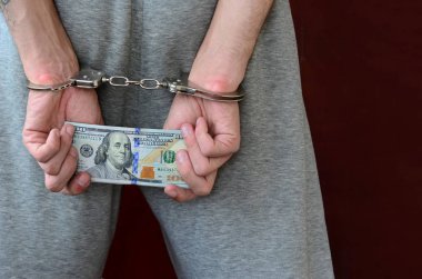 Kelepçeli elleriyle gri pantolon tutuklanan bir adam para büyük miktarda tutar. Arkadan görünüm.