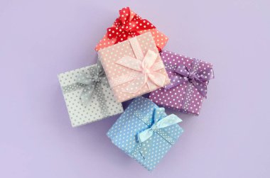 Küçük renkli hediye kutuları şeritler yığını mor bir arka plan üzerinde yatıyor. Üstten görünüm minimalizm düz yatıyordu.