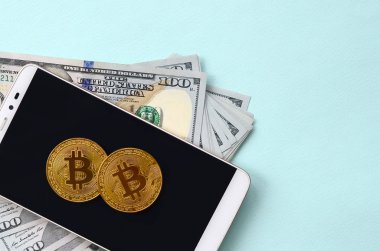 Bir akıllı telefon ve açık mavi arka planı üzerinde yüz dolar faturaları üzerinde Bitcoins yalan.