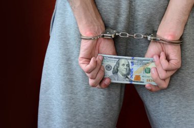 Kelepçeli elleriyle gri pantolon tutuklanan bir adam para büyük miktarda tutar. Arkadan görünüm.