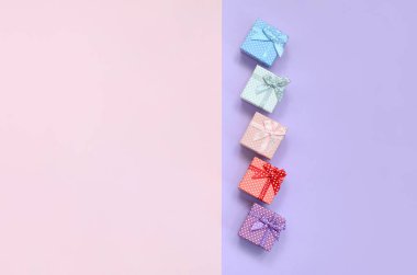 Küçük hediye kutuları farklı renklerde kurdeleler yalanlar üzerine mor ve pembe renkli bir arka planla ile.