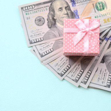 Yüz dolar faturaları üzerinde bir açık mavi renkli yakınındaki pembe noktalı hediye kutusu yatıyor.