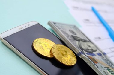 Vergi formları, yüz dolar faturaları ve açık mavi renkli smartphone ile Bitcoins yatıyor. Gelir vergisi beyannamesi.