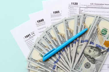 Tax forms lies near hundred dollar bills and blue pen on a light blue background. Income tax return. clipart