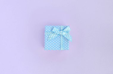 Küçük mavi hediye kutusu kurdele ile mor bir arka plan üzerinde yatıyor. Üstten görünüm minimalizm düz yatıyordu.