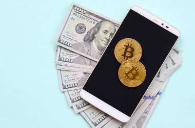 Bir akıllı telefon ve açık mavi arka planı üzerinde yüz dolar faturaları üzerinde Bitcoins yalan.